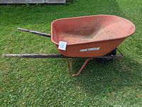Side profile of orange True Temper wheelbarrow showing metal tray, wood handles, steel legs, pneumatic wheel
