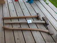 Three striking tools side by side on deck boards: two axes, one sledgehammer