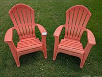 Two matching coral plastic Adirondack chairs on lawn