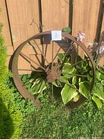 Full view of rusted spoked steel wheel rim leaning against fence