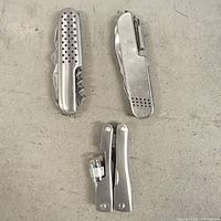 All items laid out: two stainless steel multi-tools, one Swiss-style with holes, one folding knife with clip, plus its detached handle halves