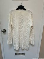 Front view of white cable knit sweater hanging