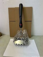 Front view of Kona Safe/Clean grill brush wrapped in plastic, showing handle, coil head, and scraper