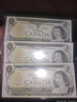 Fronts of three sequential Bank of Canada $1 bills in plastic holders