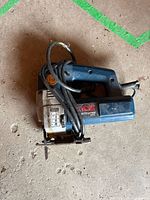 Full view of Ryobi corded jigsaw, cord wrapped around handle, blade visible