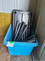 Blue recycling bin holding stacked black plastic shelves and round posts