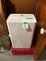Front and side view of white NOMA dehumidifier on crate with green drain hose