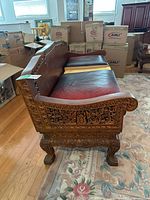 Side view of carved teak bench with leather cushion remnants showing carved arm, apron and legs