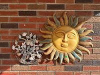 Metal sun and tree plaque hanging on brick wall