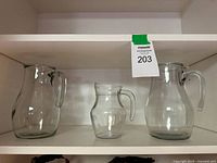 Three clear glass pitchers on shelf