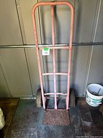front view of pink steel hand truck showing frame, handle, wheels and rusted toe plate