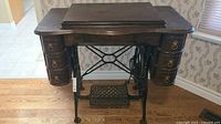 Front view of treadle sewing machine cabinet showing drawers and pedal