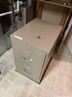 Full view of beige two-drawer metal filing cabinet with key on top