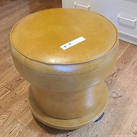 Front view of round ochre vinyl sewing stool on casters