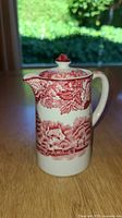 Front view of red transferware jug with lid showing pastoral scene
