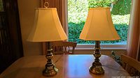 Two brass table lamps with shades on table