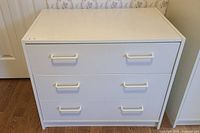 Front view of white three-drawer dresser with handles visible