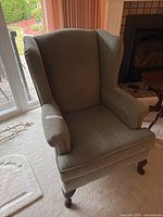 Front view of green wingback chair showing upholstery, arms, seat cushion and legs
