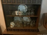 Cabinet view showing assorted glasses, mugs, plates and pitcher
