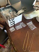 Box with numerous bagged costume jewellery and two gold-tone chains laid out