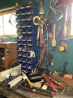 Overview showing wall-mounted blue bins, hanging hand tools, paint roller, caulk gun, sprayer, cast iron pan partly visible