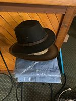 Black Australian Outback hat stacked on brown straw hat resting on packaged blue shirts