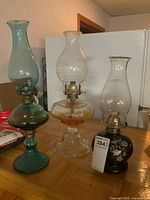Three oil lamps side by side on table showing overall condition and design
