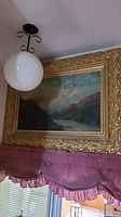 Full view of framed landscape oil painting mounted above window treatment