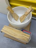 White ceramic bowl holding two wooden paddles; sealed nine-piece spatula set beside it