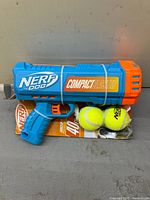 Front view of Nerf Dog Compact Ball Blaster on retail card with two tennis balls