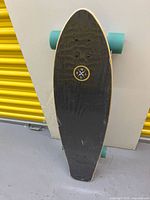 Top of skateboard showing black grip tape and logo, shrink-wrap in place