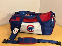 Side view of blue/red/white Chicago Cubs duffel with shoulder strap and MLB tag attached