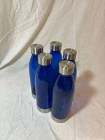 Front angle showing five blue bottles with stainless caps and bases