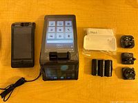 All components laid out: handheld terminal, printer dock, AC adapter, plug heads, thermal rolls, sealed cradle