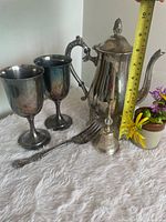 Group shot showing coffee pot, two goblets, serving fork, bell with measuring tape for scale