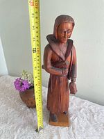 Full view of carved wood figure with measuring tape showing height
