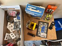 Overview of lot showing wire coil, electrical wall plates, painting items, grille panel, licence plate, tape measure and remote