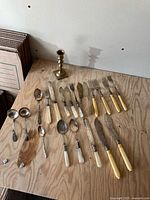 Full lot layout on plywood surface showing all flatware pieces and candlestick