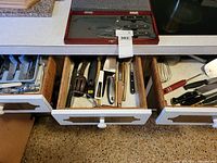 Overview of three open kitchen drawers showing flatware tray, utensils and boxed knife set