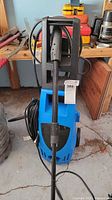 Front view of blue Pacific Hydrostar pressure washer showing wand, hose and power cord