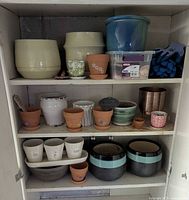Cabinet shelves displaying assorted glazed and terracotta pots, saucers, clear bin and gloves