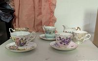 Group view of all four teacup & saucer sets plus creamer