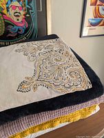 Stacked textiles showing patterned shower curtain, navy fleece, lavender and yellow blankets, and part of white duvet