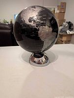 Full view of black globe showing Americas, silver landmasses, chrome base