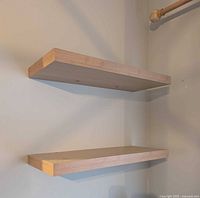 Two light natural wood floating shelves mounted on wall