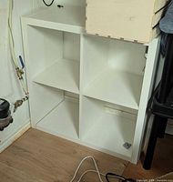 Front view of white IKEA KALLAX 2x2 cube shelf showing four compartments and visible wear near base
