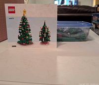 Instruction booklet for LEGO Christmas Tree set 40573 alongside plastic tub containing loose bricks