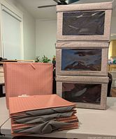 Stack of three grey windowed boxes next to five folded peach bins