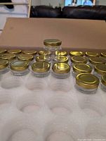 Open box showing rows of clear glass jars with gold lids seated in foam tray