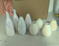Eight small pearl-white iridescent ceramic bud vases, front view